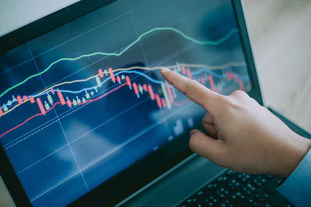 Hand pointing at stock market graph on laptop screen