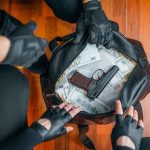 Gloved hands around bag with money and gun