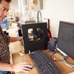 Man operating 3D printer and computer workstation