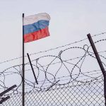 Barbed wire fence with Russian flag in background