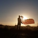 Silhouette holding USA flag against sunset sky