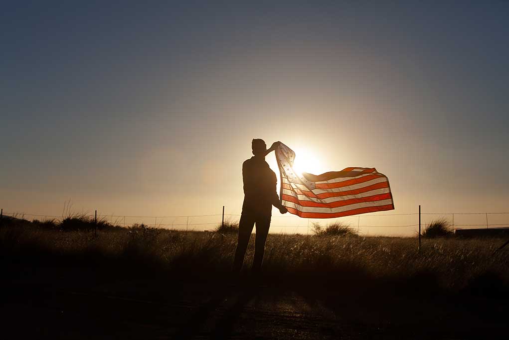 Silhouette holding USA flag against sunset sky