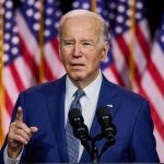 Man speaking at podium with American flags behind