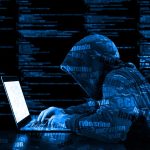 Hooded figure using laptop with code background