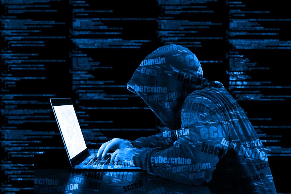 Hooded figure using laptop with code background