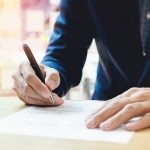 Person signing a document with a pen