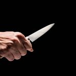 Hand holding a knife against a black background
