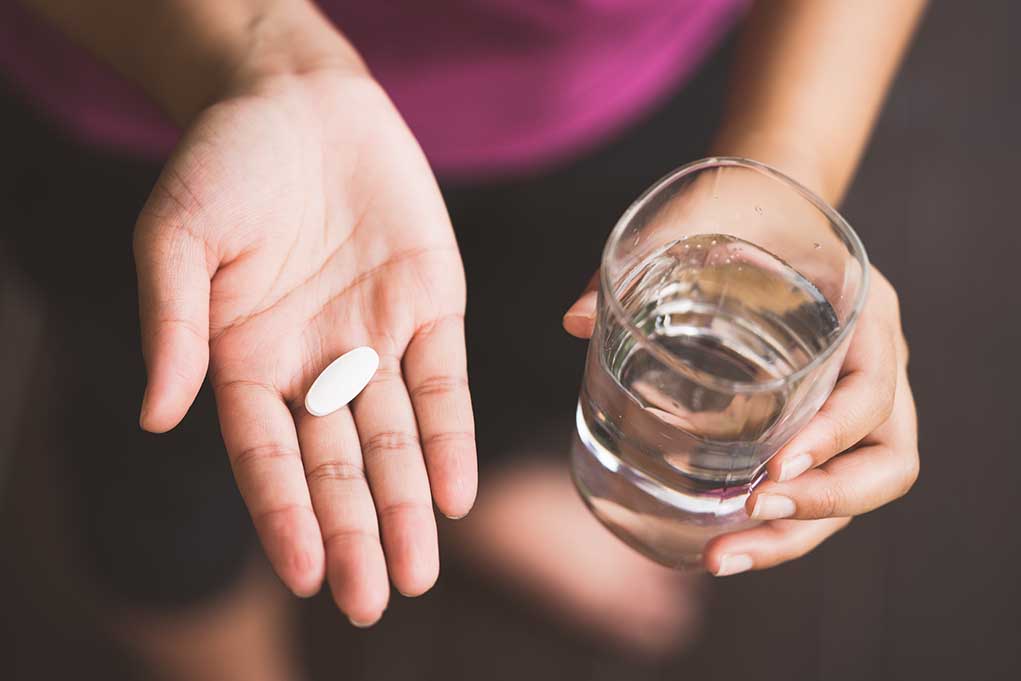 Person holding pill and glass of water