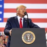 Man speaks at podium with US flag background