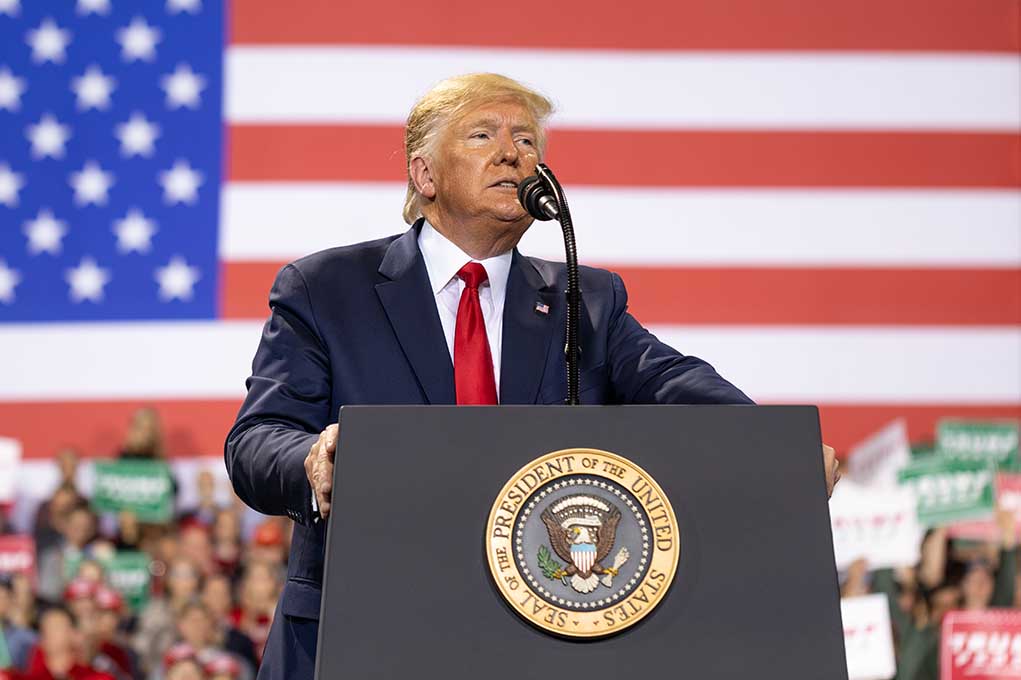 Man speaks at podium with US flag background