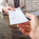 Hands exchanging a check near a laptop