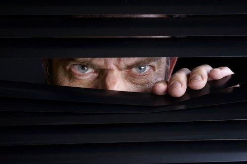 shutterstock_266683784.jpg featured image Man peeking through half-open black blinds.