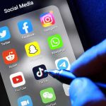 Explosive Report: Russian Agents PREY on Broke Teens Social media apps on phone screen with hand holding stylus