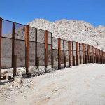 Floating Border Wall SHOCKS—Billions at Stake A long border wall stretches across a desert landscape with mountains in the background