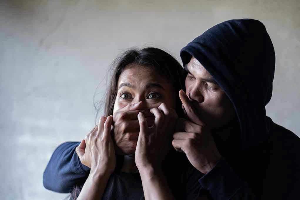 1381990856 Man holding woman's mouth, gesturing silence.