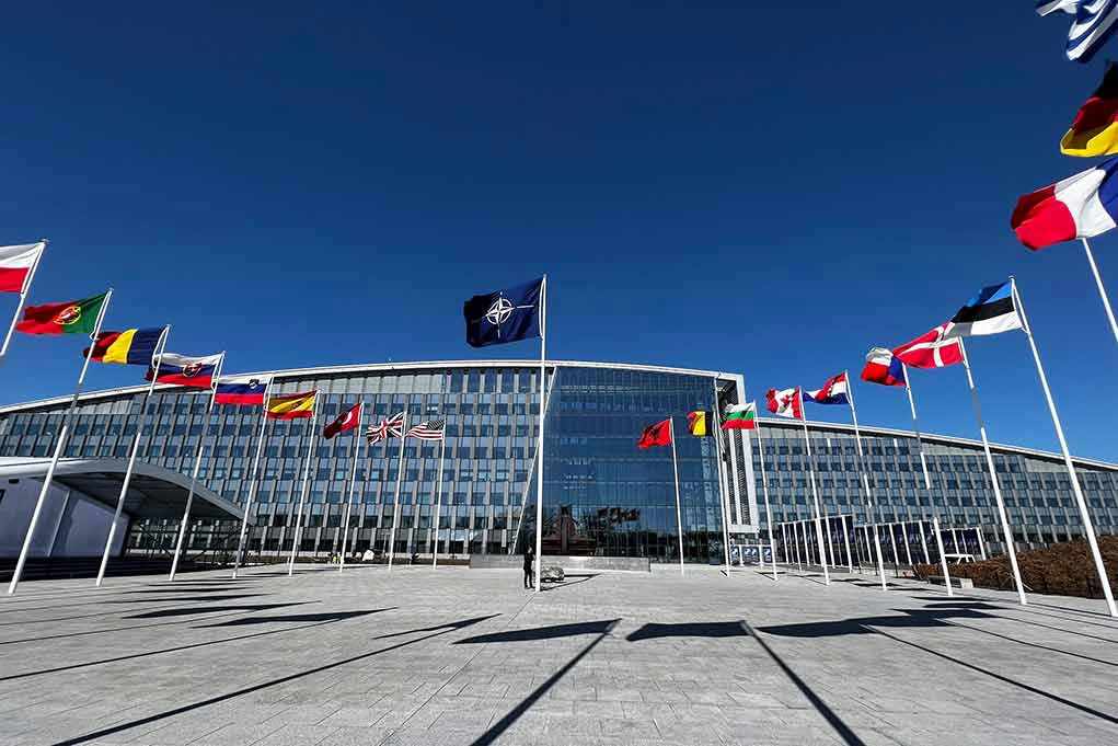 Flags outside NATO headquarters building under clear blue sky