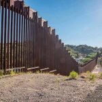 TRUMP’S Black Wall Move Stuns Border States Tall metal border wall with rural landscape.