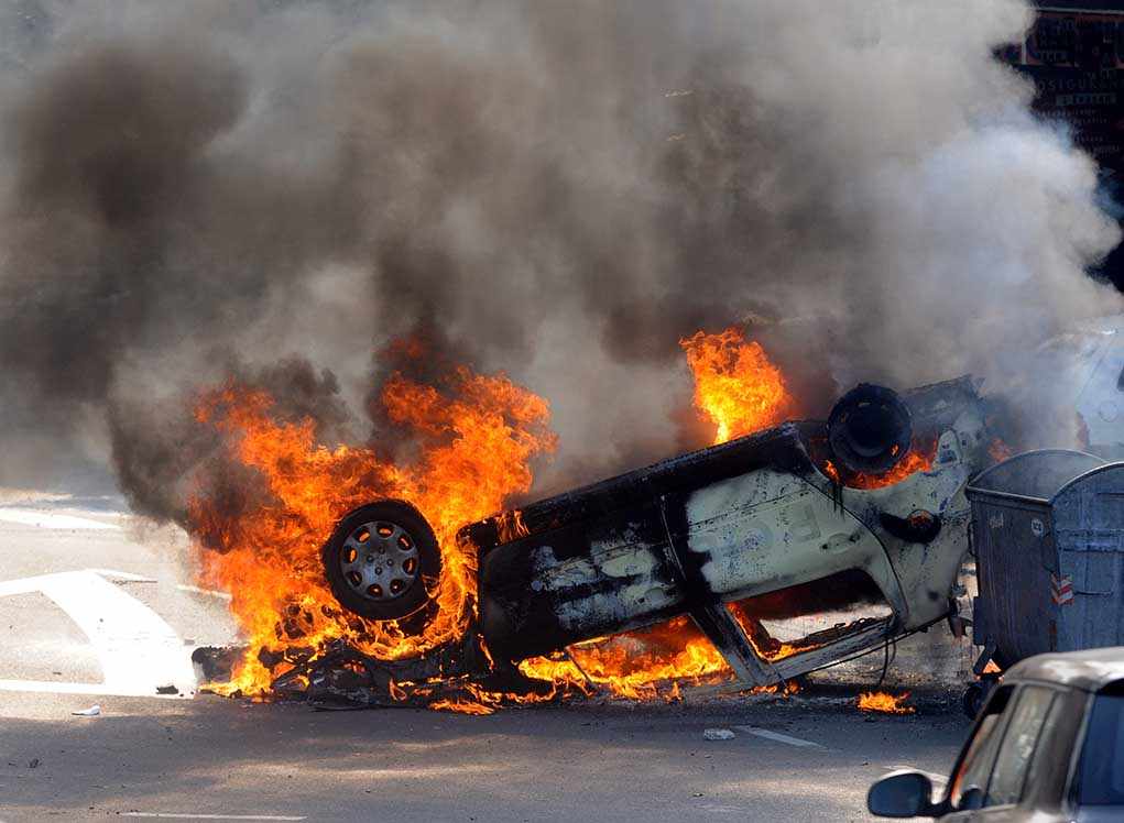 shutterstock_137895923.jpg An overturned car engulfed in flames and smoke on a city street