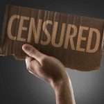 A hand holding a cardboard sign that reads CENSORED