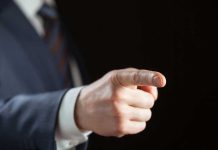 BRAIN ANEURYSM Strikes Celebrity — Doctors Place Shocking Blame Person pointing with finger, wearing a suit.