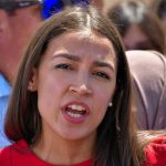 Raging Sanders-AOC Clash Stuns Live TV Woman speaking to a crowd outdoors.