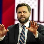 VP Vance Watches EXPLOSIVE Military Catastrophe Man in suit gesturing with hands on stage.