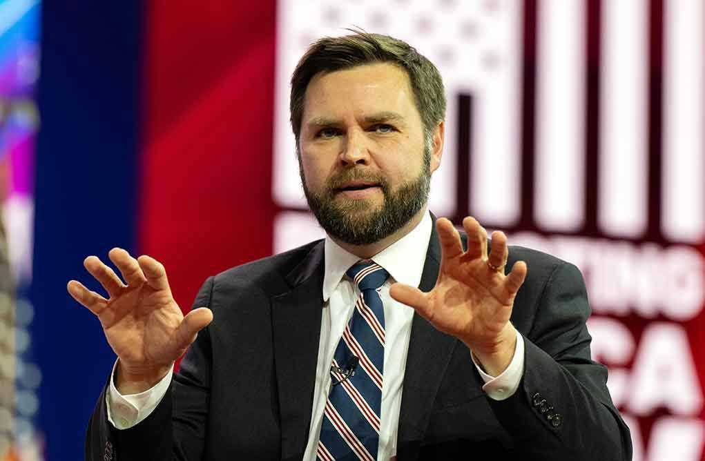 Man in suit gesturing with hands on stage.