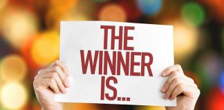 Hands holding a sign reading The Winner Is...