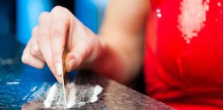 A hand using a card to prepare a line of white powder on a reflective surface
