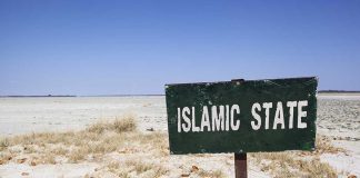 A weathered sign reading 'ISLAMIC STATE' in a barren landscape