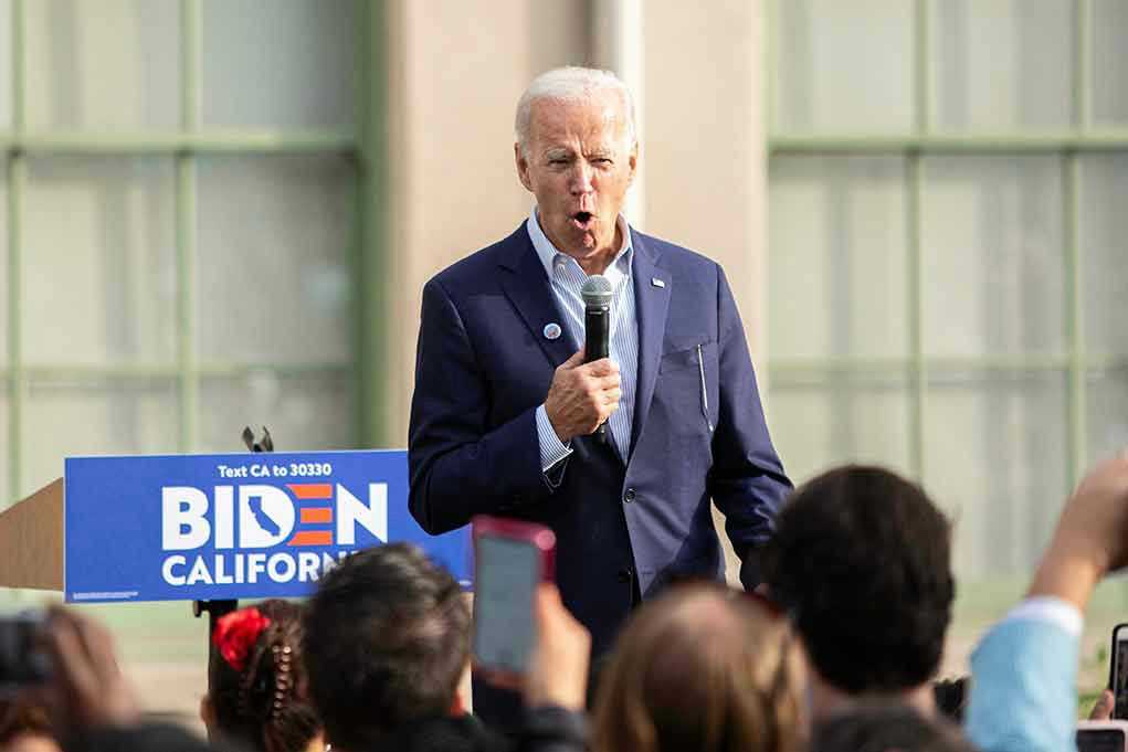 Man speaking at an outdoor event with Biden sign.
