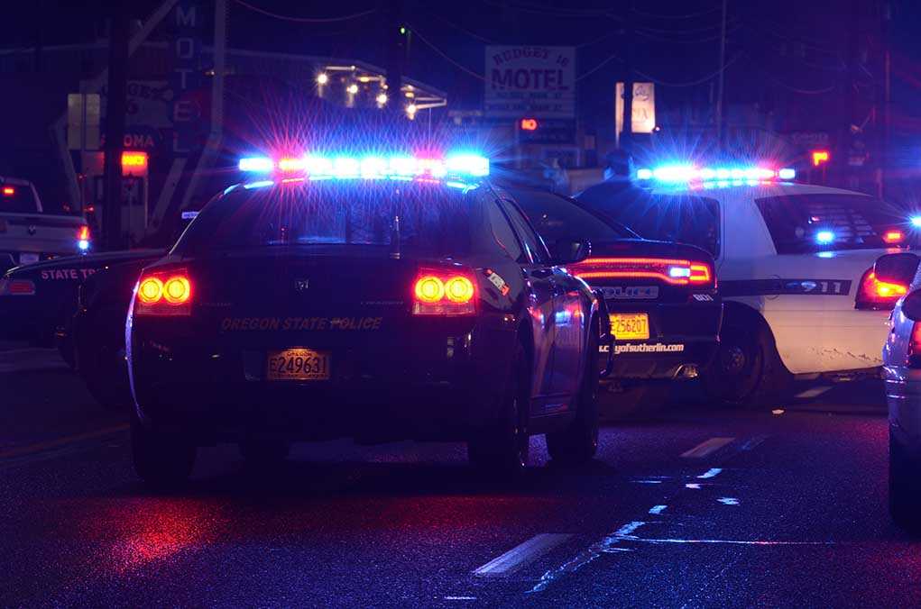 Police cars with flashing lights at a nighttime scene near a motel