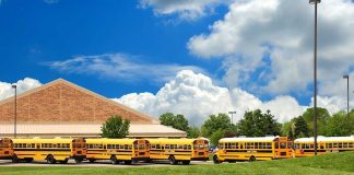 A row of yellow school buses parked in front of a school building under a cloudy sky