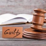 A wooden gavel next to a card that reads 'Guilty' and an open book