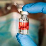 Gloved hand holding vial with red liquid and flag.