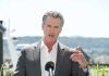 Terrifying Newsom Blueprint Targets Trump Agenda Man speaking with microphone outdoors.