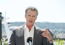 Terrifying Newsom Blueprint Targets Trump Agenda Man speaking with microphone outdoors.