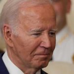 J6 Pipe Bomb Arrest: Biden Incompetence Exposed Man in a suit looking thoughtful.