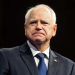 Conservatives SLAM Walz’s “Violence” Overreaction Man in suit with a U.S. flag pin.