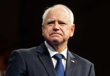 Conservatives SLAM Walz’s “Violence” Overreaction Man in suit with a U.S. flag pin.