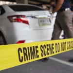 Crime scene tape blocking off white sedan.