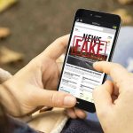 Person holding smartphone displaying fake news notification.
