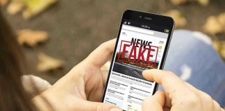 Person holding smartphone displaying fake news notification.