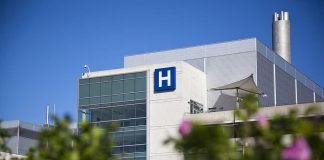 Modern hospital building with a prominent H sign against a clear blue sky