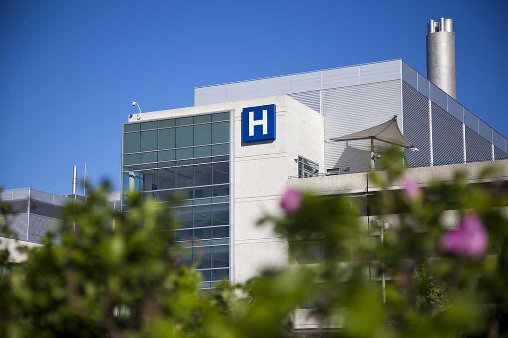 Modern hospital building with a prominent H sign against a clear blue sky