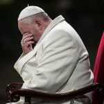 Pope sitting with his head bowed and hand covering his face