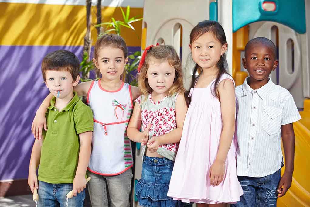 Five children standing together in a playground setting, smiling at the camera