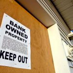 Sign on a boarded-up property indicating it is bank owned and warns to keep out