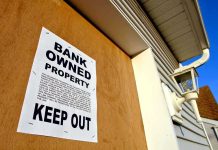 Sign on a boarded-up property indicating it is bank owned and warns to keep out