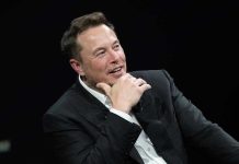 Musk Goes NUCLEAR After Trump Feud Man in suit smiling, resting chin on hand.
